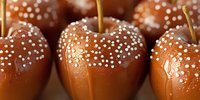 Caramel covered apples decorated with white sugar crystals on brown background, close up macro shot showing glossy coating and delicate sprinkles.