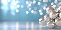 Shiny silver Christmas baubles arranged in cluster against blurred blue bokeh background with reflective surface, creating festive holiday atmosphere.