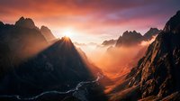Dramatic mountain valley landscape with golden sunrise light breaking through misty peaks and winding river below, suitable for travel, nature, and editorial projects.