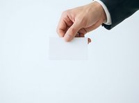 Caucasian male hand in dark business suit holding blank white card against neutral background for corporate messaging and branding.