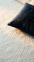 Black decorative pillow with quilted geometric pattern resting on white textured mattress surface. Suitable for home decor, bedding, and interior design projects.