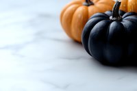 Black and orange decorative pumpkins on white marble background with copy space. Modern minimal autumn holiday composition for seasonal design.