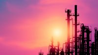Industrial refinery silhouettes against vibrant purple and orange sunset sky with bright sun creating dramatic atmospheric scene for environmental concepts.