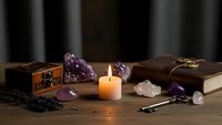 Mystical altar setup with burning candle, amethyst crystals, vintage books, ornate wooden box and ritual tools on dark wooden surface for spiritual practices.