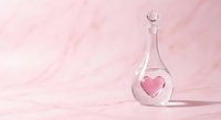 Glass flask with pink heart inside on soft pink marble background for romantic chemistry and love potion concepts in laboratory setting.