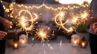 Hands holding lit sparklers with glowing bokeh lights and candles in soft focus background, celebrating festive occasions and special events.