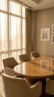 Modern conference room with round wooden table and beige chairs bathed in warm natural sunlight from large windows for business meetings.