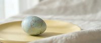 Painted Easter egg with delicate floral pattern resting on wooden spoon, soft natural lighting creates peaceful spring holiday atmosphere for seasonal decor.