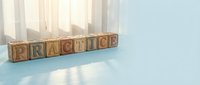 Wooden alphabet blocks spelling PRACTICE on light blue surface with soft natural lighting from window creating warm shadows for educational content.