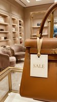 Luxury tan leather handbag with gold hardware and sale tag in an elegant boutique interior with soft beige tones.