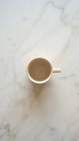 Empty beige ceramic coffee mug on white marble surface from above. Minimalist kitchen flatlay for morning beverage concepts and cafe branding materials.