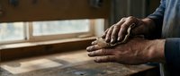 Elderly man's weathered hands resting on wooden table by window, showcasing life experience and wisdom in warm natural lighting for healthcare concepts.
