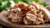Pulled pork with barbecue sauce on wooden plate, slow cooked shredded meat for sandwiches and meals, comfort food ready to serve.