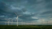 Wind turbines generating renewable energy across vast green field under dramatic stormy sky, suitable for sustainable energy, environmental technology, and clean power industry projects.
