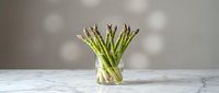 Fresh green asparagus spears in glass vase on marble counter, healthy organic vegetable ingredient for gourmet cooking and spring recipes.
