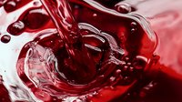 Dynamic splash of red wine pouring into glass creating swirling liquid motion with bubbles and ripples against white background, macro photography for beverage advertising.