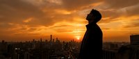 Silhouette of contemplative man against dramatic orange sunset sky overlooking urban cityscape from rooftop, perfect for motivation and success concepts.