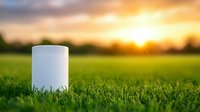 White cylindrical container on green grass against dramatic sunset sky with golden sunlight, nature background for eco-friendly product packaging presentation.