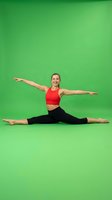 Young Caucasian woman in red sports bra performing split stretch on green background. Fitness instructor demonstrating flexibility exercise for wellness content.