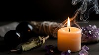 Mystical candle flame with smoke surrounded by amethyst crystals and spiritual tools on dark wooden surface for meditation and healing rituals.