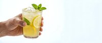Fresh lemonade with mint leaves and ice cubes held by hand against white background. Summer refreshing drink for restaurants and beverage marketing.