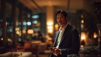 Professional businessman in suit using smartphone in upscale restaurant or hotel lobby with warm ambient lighting and bokeh background at night.