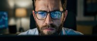 Man with glasses focused on computer screen, reflecting digital code and data analysis in lenses, representing programmer, developer, or IT professional working on software development.