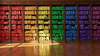 Rainbow colored books arranged by hue on wooden library shelves creating vibrant spectrum display for education and learning concepts.