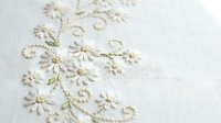 Delicate white and gold floral embroidery on cream fabric with intricate stitching and beadwork details for luxury textile and fashion design projects.
