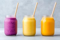 Fresh fruit smoothies in mason jars with paper straws - purple berry, banana mango and orange carrot drinks on light gray background for healthy breakfast.