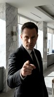 Confident middle-aged Caucasian businessman in black suit pointing at camera in modern marble office interior with city view windows for corporate leadership concepts.
