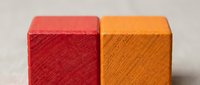 Two colorful wooden blocks with textured diagonal line patterns in red and orange colors on neutral background for educational toys and crafts.