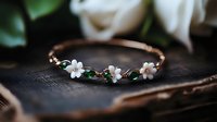 Elegant rose gold bracelet with delicate flower charms and green gemstones on vintage book with white roses in romantic setting for jewelry photography.
