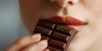 Woman with red lipstick holding dark chocolate bar close to lips, sensual eating concept for food photography and lifestyle advertising campaigns.