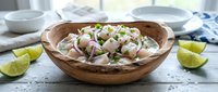 Fresh ceviche with white fish, red onions and cilantro served in wooden bowl with lime wedges on rustic white table for Latin American cuisine recipes.