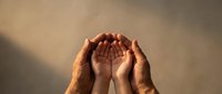 Adult hands protectively cupping child hands in prayer position against warm beige background symbolizing family protection and spiritual guidance.