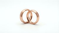 Two elegant rose gold wedding rings interlinked together on white background, symbolizing love, commitment and marriage union for couples.