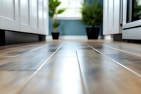 Low angle view of modern kitchen floor with wooden tiles, white cabinets and potted plants in background. Selective focus creates depth perspective.