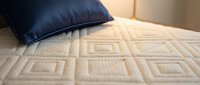 Quilted beige mattress with geometric diamond pattern and navy blue pillow, suitable for bedroom interior design and home decor projects.