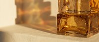 Golden amber glass bottles with ice cubes on neutral surface, suitable for beverage, perfume, and luxury product packaging design mockups.
