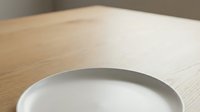 Empty white ceramic plate on light wooden table surface, suitable for food photography, restaurant menus, and dining concepts.