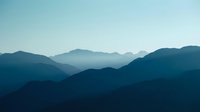 Layered mountain silhouettes fade into misty distance under clear sky, conveying depth and tranquility for nature, travel, and landscape design projects.