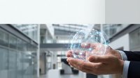Young professional male with medium skin tone holding glowing digital network sphere in cupped hands against modern office building backdrop, representing technology innovation and business connectivity.
