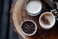 Coffee beans, milk and cappuccino on wooden tray. Morning beverage preparation with roasted beans and frothy drink for cafe menu design.