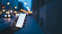 Hand holding smartphone with blank white screen at night on city street with blurred lights background for mobile app mockup and digital technology concepts.