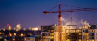 Construction site with tower crane building modern residential apartments at twilight with city lights bokeh background for urban development projects.