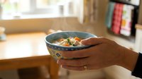 Hands holding a steaming bowl of homemade chicken vegetable soup in a cozy kitchen, warm comfort food concept.