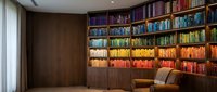 Modern home library with color-coordinated books arranged by rainbow spectrum on built-in wooden shelves creating organized literary collection display.