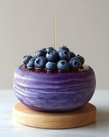 Fresh ripe blueberries in purple ceramic bowl on wooden stand against neutral background, minimalist food styling for healthy eating and dessert concepts.