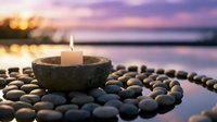 Zen meditation candle burning in stone bowl surrounded by smooth pebbles at peaceful lakeside during sunset creating tranquil spa atmosphere for relaxation and mindfulness.